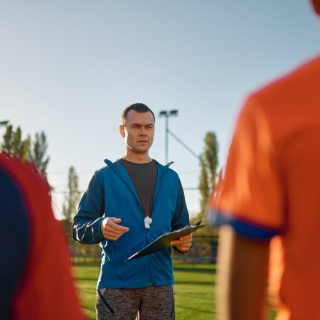 Young soccer coach teaching kids on football field